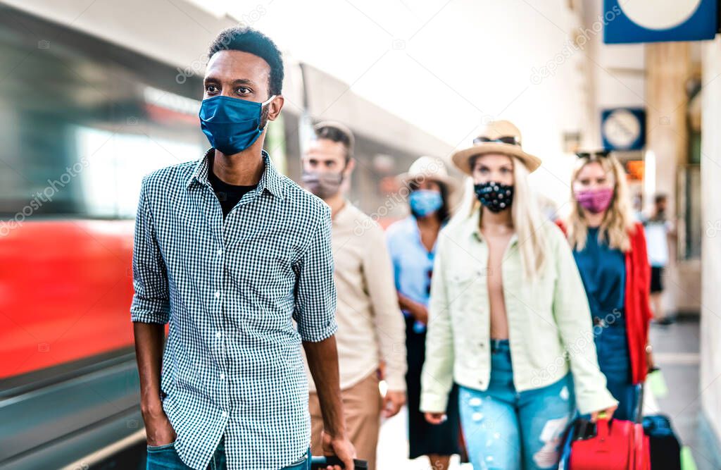 Multiracial crowd of people walking at railway station platform - New normal travel concept with young travelers covered by protective face mask - Focus on african american guy at left