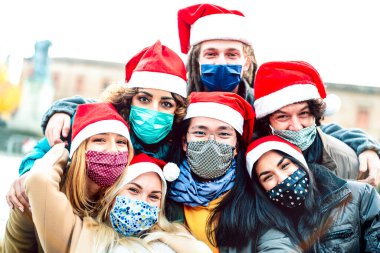 Yüz maskesi ve Noel Baba şapkası takarak selfie çeken çok ırklı arkadaşlar, açık havada eğlenen gençlerin olduğu yeni bir Noel konsepti.