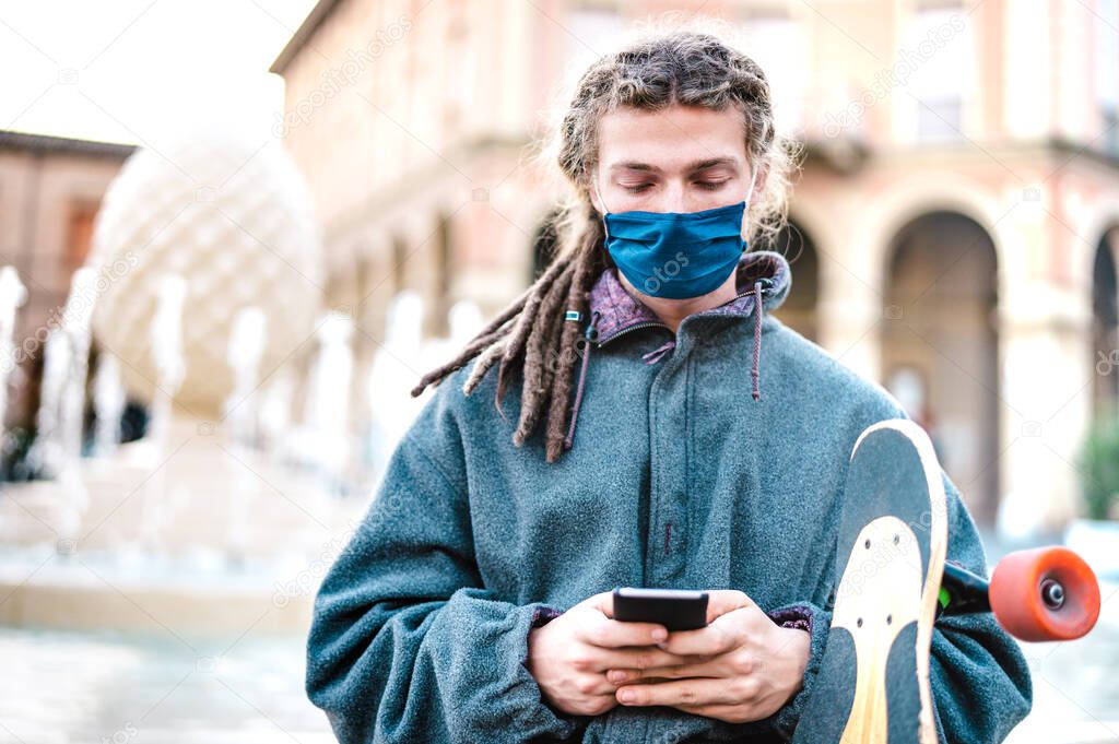 Unhappy guy with protective mask using tracking app on mobile smartphone - Young worried millenial sharing content on social media - New normal lifestyle concept - Bright filter with focus on face