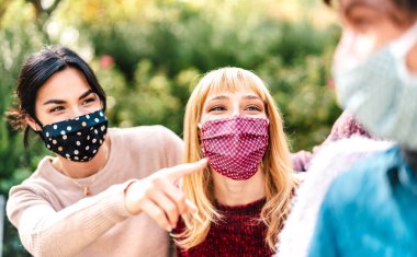 Yüz maskesi takarak eğlenen genç çok ırklı insanlar - mutlu arkadaşlarla parkta boş vakitlerini paylaşan yeni normal yaşam tarzı konsepti - orta kadın gözlerine odaklı sıcak, parlak bir filtre