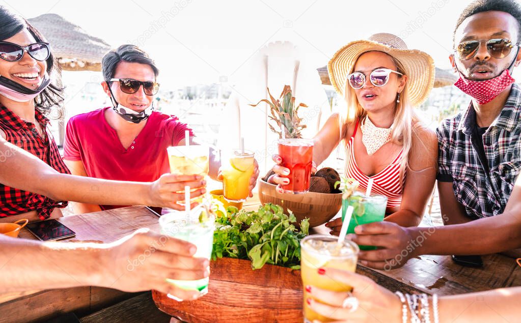 Young multicultural people toasting at beach cocktail bar with open face mask - New normal summer concept with milenials having fun together cheering drinks - Vivid filter with focus on girl with hat