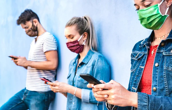 Milenial friends using mobile phone covered by face mask - Young people sharing content on cellphone - New normal concept about always connected teenager - Vivid azure filter with focus on right hands