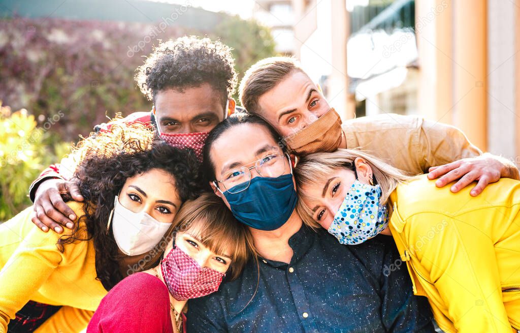 Multicultural milenial friends taking selfie smiling behind face masks - New normal friendship and life style concept with young people having fun together outside - Warm bright vivid filter