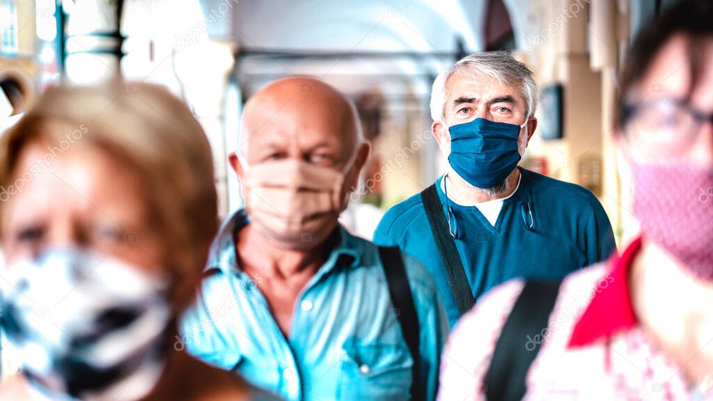 Urban crowd of adult citizens walking on city street during pandemic - New reality life style concept with senior people with covered faces - Selective focus on bearded man with blue protective mask