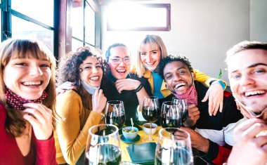 Friends taking selfie at winery bar drinking wine glass with open face mask - People having fun together at restaurant reopening - Selective focus on middle guys and girls with bright backlight filter clipart