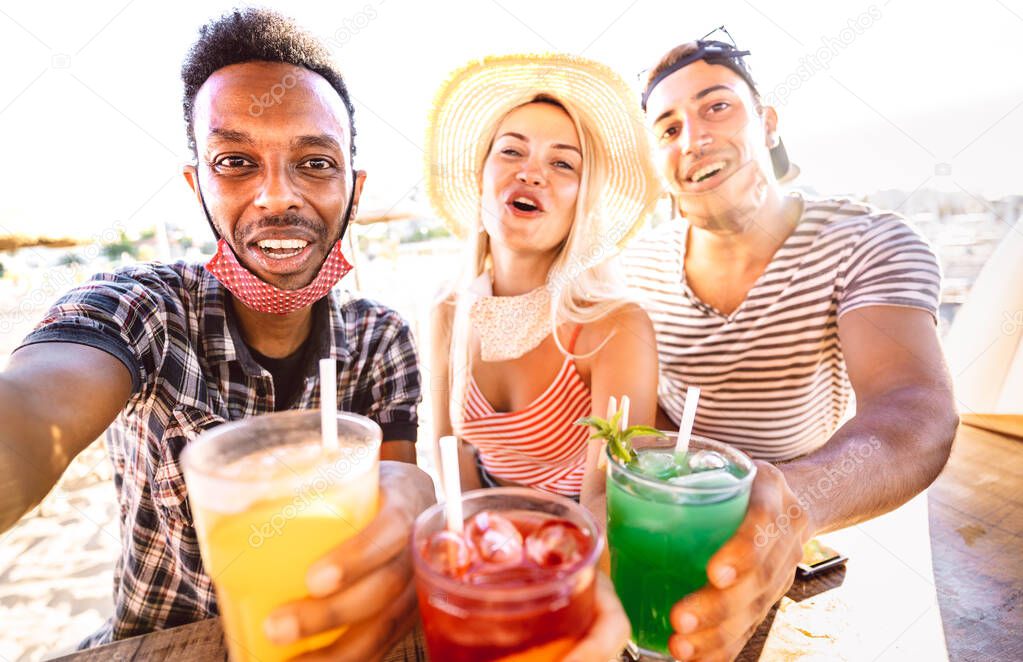 Multiracial people trio taking selfie with open face masks at beach bar - New normal life style concept with drunk friends having fun together at summer resort vacation - Bright warm backlight filter