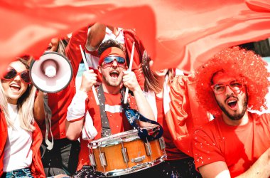 Futbol taraftarları, stadyum tribününde futbol kupasının maçını izlerken bayrak sallayarak tezahürat yapıyorlar - Kırmızı tişörtlü gençler grubu spor şampiyonasında eğleniyorlar