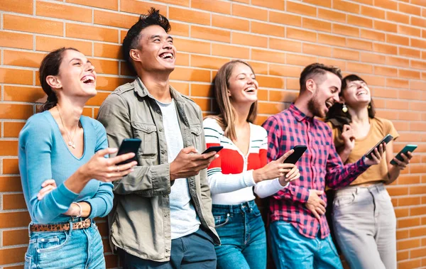 大学のキャンパスの壁にスマートフォンを使って笑っている多文化の友達 携帯電話で中毒の若者 常に接続されたミレニアルと技術の概念 鮮やかなフィルター — ストック写真
