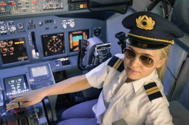 Beautiful blonde woman pilot wearing uniform and hat with golden wings - Modern aircraft cockpit ready for take off - Concept of female emancipation clipart