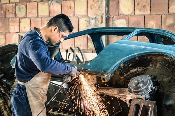 Young man mechanical worker repairing an old vintage car body in messy garage - Safety at work with protection wear — Stock Photo, Image