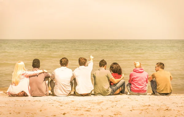 Groep internationale multiraciale vrienden zitten op het strand met elkaar praten en overweegt de zee - Concept van multi culturele vriendschap tegen racisme - warme vintage gefilterde look — Stockfoto