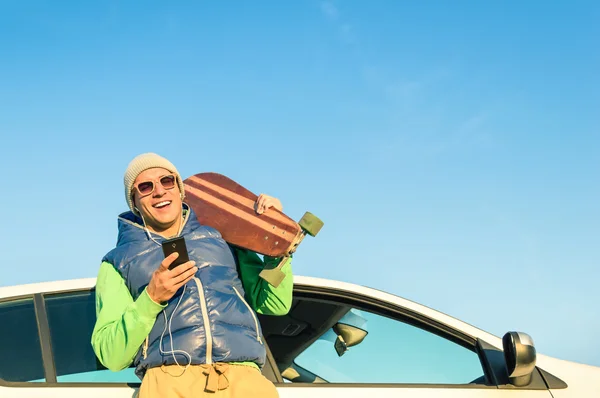 Unga hipster man med smartphone lyssnar musik nästa hans bil - konceptet med modern teknik blandat med en vintage travel livsstil - höst vinter ungdom alternativt mode i en solig dag resa — Stockfoto