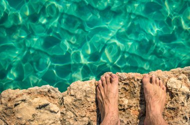 Naked human barefoot on rock cliff ready to jump in the clear blue water - Comino and Gozo blue lagoon in Malta - Freedom and carefree lifestyle during travel and vacation in exclusive destinations clipart