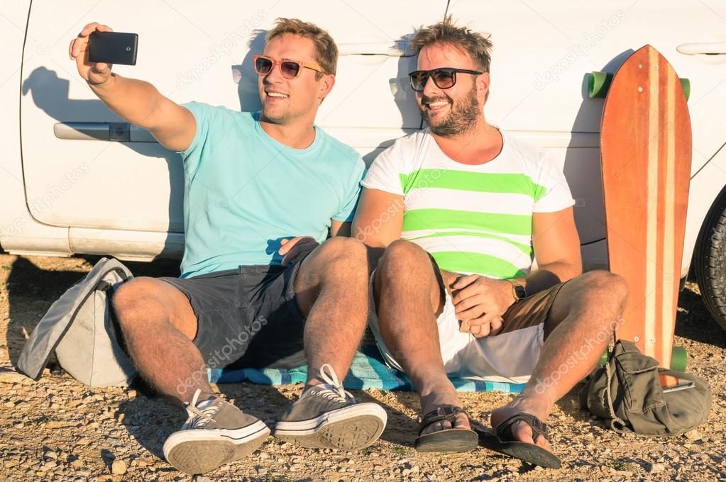 Young hipster best friends taking a selfie sitting next to the car - Concept of modern technologies mixed with vintage lifestyle - Adventurous friendship during travel and