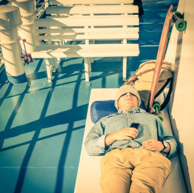Dünya çapında backpacking smartphone - özgürlük ve alternatif yaşam tarzının Modern kavram - ucuz seyahat tutan bir feribot tekne geçiş sırasında bir dinlenme sahip genç hipster adam
