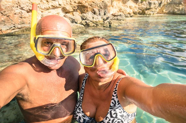 Senior happy couple taking a selfie at Blue Lagoon in Gozo and Comino - Travel to mediterranean island of Malta - Concept of active elderly and fun around the world experimenting new technologies