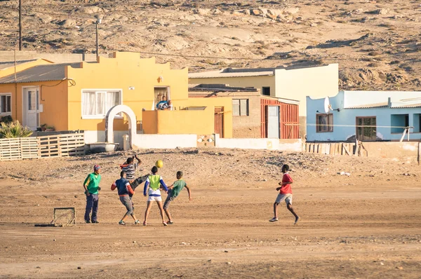 Lüderitz, Namibia - 24 listopada 2014: lokalnych młodych ludzi gry w piłkę nożną na placu zabaw obok nowoczesnych township. Na szczęście i utalentowanych graczy piłka nożna jest szybkim sposobem ucieczki ubóstwa slumsów — Zdjęcie stockowe