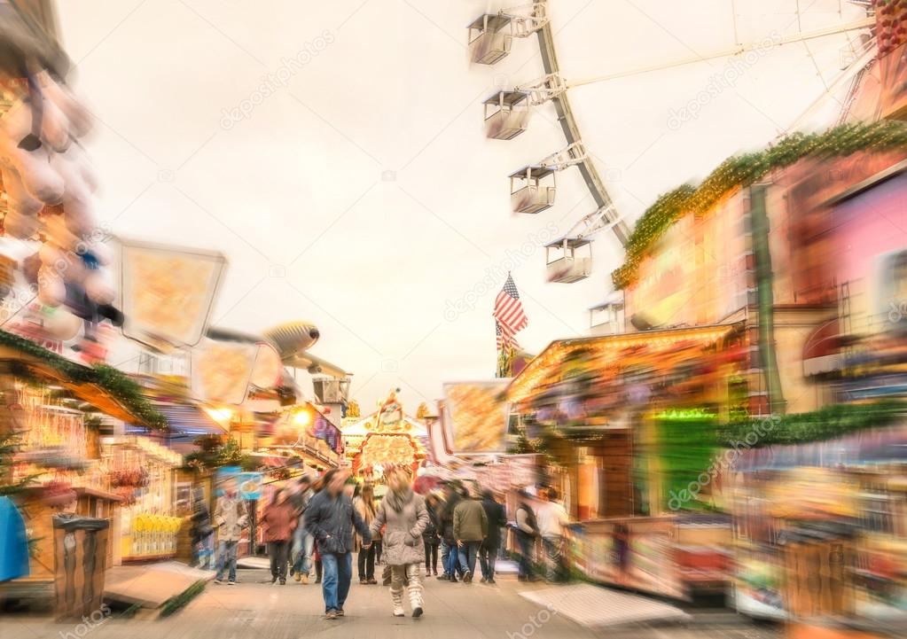 Crowd of people walking at luna park on a radial zoom defocusing - Multicolored fun stands at german Christmas market - Ferris wheel and colorful wooden houses at Berlin amusement area in winter time
