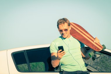 Akıllı telefon dinleme müzik gezisi sırasında genç hipster adamla zorla sonraki arabasını - yeni eğilimler ve modern teknolojiler ile bir retro yaşam tarzı - yumuşak karışık kavramı vintage bir filtre uygulanmış görünüm desaturated