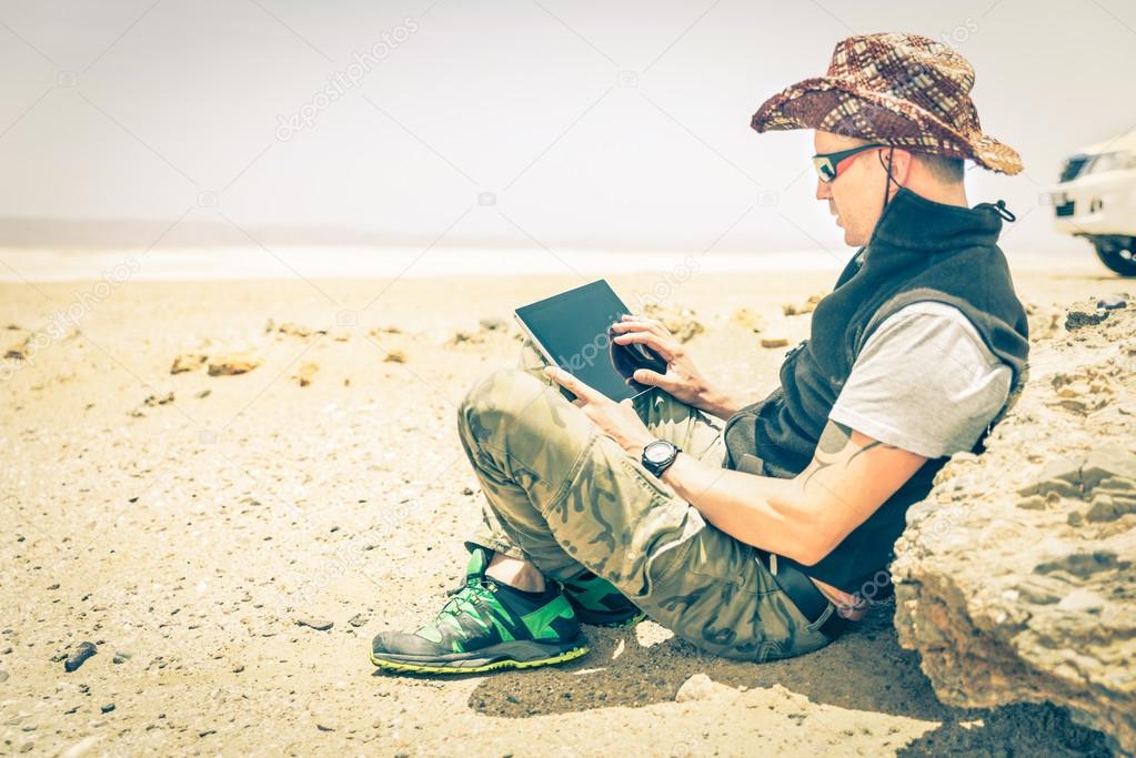 Young hipster man sitting in desert road - Concept of modern technologies with a alternative travel lifestyle - Overexposed vintage desaturated filtered look with focus on the hand using the laptop