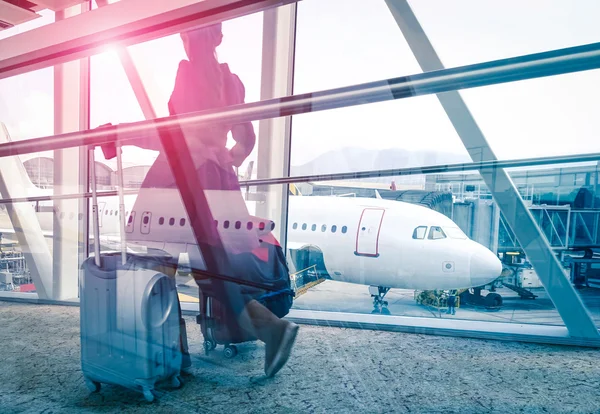 Concepto de viaje con mujer y maleta moviéndose rápido a la puerta de la terminal del aeropuerto - Aspecto de doble exposición con enfoque en el avión en el fondo - Bengala de sol de marsala violeta con edición filtrada vintage — Foto de Stock