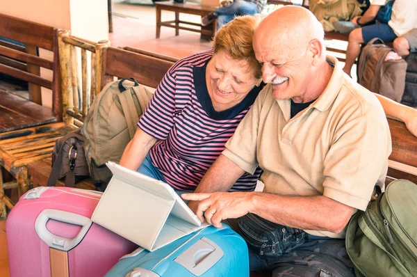 Feliz pareja de ancianos sentados con portátil digital y equipaje de viaje durante el viaje de aventura alrededor del mundo - Concepto de estilo de vida activo de los ancianos y la interacción con nuevas tendencias y tecnologías —  Fotos de Stock