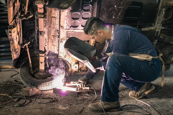 Young man mechanic worker repairing old vintage car body in messy garage - Safety at work and protection wear - Guy with cool hair cut at vehicle renovation - Soft focus with natural light lens flare — Stock Photo, Image