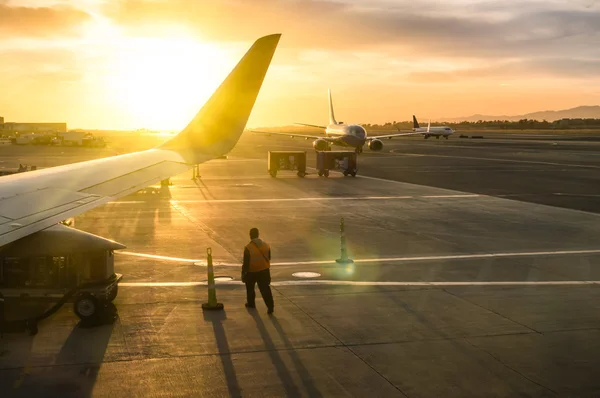 Homem trabalhador caminhando perto da asa do avião no portão terminal do aeroporto internacional durante o pôr do sol - Conceito de viagem emocional ao redor do mundo - Foco suave e brilho da lente solar devido à retroiluminação — Fotografia de Stock