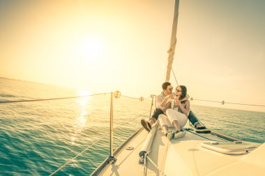 Young couple in love on sail boat with champagne at sunset - Happy exclusive alternative lifestye concept  - Soft focus due to backlight on vintage nostalgic filter - Fisheye lens and tilted horizon