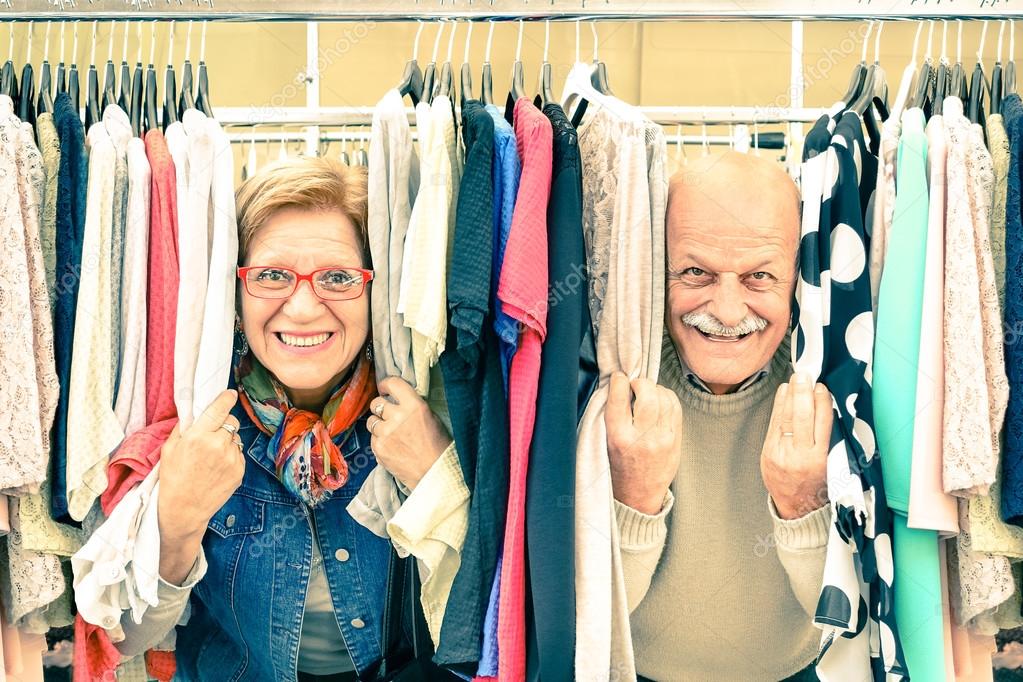 Playful senior couple at weakly flea market - Concept of active elderly with mature man and woman having fun and shopping in the old town - Happy retirement moments on a warm vintage nostalgic look