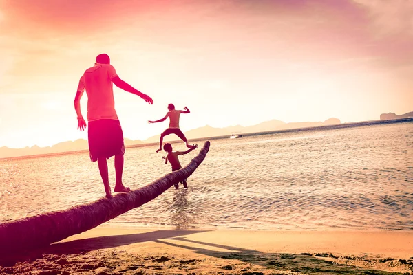 Father playing with sons at tropical beach with tilted horizon - Concept of  family union with man and children having fun together - Modified unrecognizable silhouettes - Marsala filtered color tones