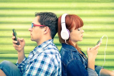 Hipster couple in disinterest moment with mobile phones - Concept of apathy sadness and isolation using new technologies - Boyfriend and girlfriend with smartphones addiction - Vintage filtered look clipart