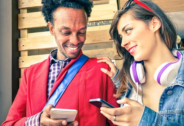 Multiracial couple flirting with smartphone numbers - Modern concept of mobile phone technology with happy people having fun - City urban lifestyle on natural light and warm vintage filtered editing — Stock Photo, Image