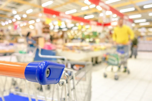 Supermercado de comestibles desenfocado borroso - Concepto de consumismo en período de crisis económica - Desenfoque vívido brillante de las personas en el centro comercial - Profundidad superficial del campo con enfoque en el borde del carrito de compras — Foto de Stock