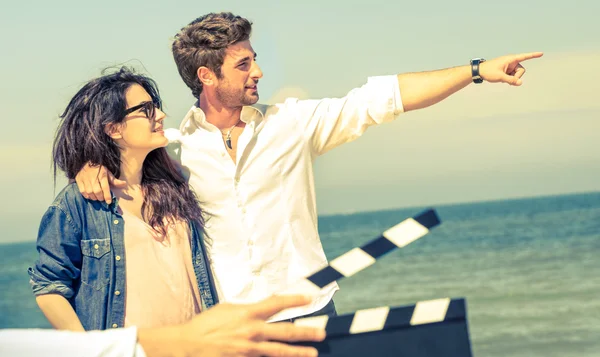 Jovem casal apaixonado atuando para filme romântico na praia - Conceito da indústria do cinema com ardósia ciak pronto para cena de filme - Estilo de vida moderno com cara confiante e namorada feliz - Foco no rosto masculino — Fotografia de Stock