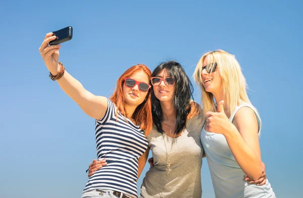 Happy girlfriends taking selfie against blue sky - Friendship summer concept with new trends and technology - Best friends enjoying moments with modern smartphone - Warm sunny afternoon color tones — Stock Photo, Image