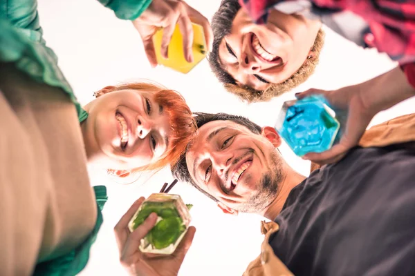 Mejores amigos en un círculo sonriendo juntos a la cámara - Jóvenes felices bebiendo cócteles multicolores - Concepto de diversión y reunión social - Profundidad superficial del campo con enfoque en los ojos del chico — Foto de Stock