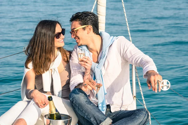 シャンパン フルート グラス - 幸せの排他的な代替 lifestye コンセプト - ボーイ フレンドとガール フレンドの高級ヨット - 日当たりの良い午後の色のトーンでいちゃつく帆ボートの愛の若いカップル — ストック写真
