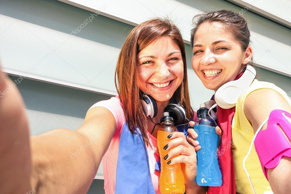 Sporty girlfriends taking selfie during a break at run training in urban area - Sport Young happy women having fun together with fitness jogging workout - Fashion sport clothes and energetic drinks