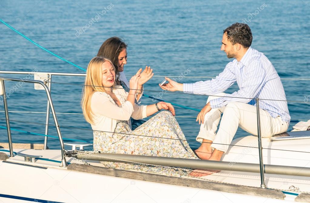 Young people having fun with smartphone on exclusive luxury sailing boat - Concept of friendship and travel with best friends interacting with new trends and technology - Late afternoon color tones