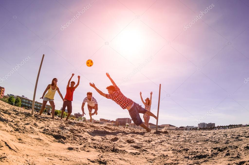 Multiracial friends playing soccer at beach - Concept of multi cultural friendship having fun with summer games - Backlight marsala filter with late afternoon sunshine halo and fisheye lens distortion