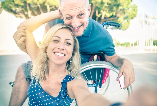 Szczęśliwa para w miłość podejmowania selfie miejskich miasta tło - niepełnosprawność pozytywne pojęcie człowieka na wózku inwalidzkim - Vintage retro filtrowane wyglądają z nieostrość na uśmiechający się kobieta z powodu słońca pochodni halo — Zdjęcie stockowe