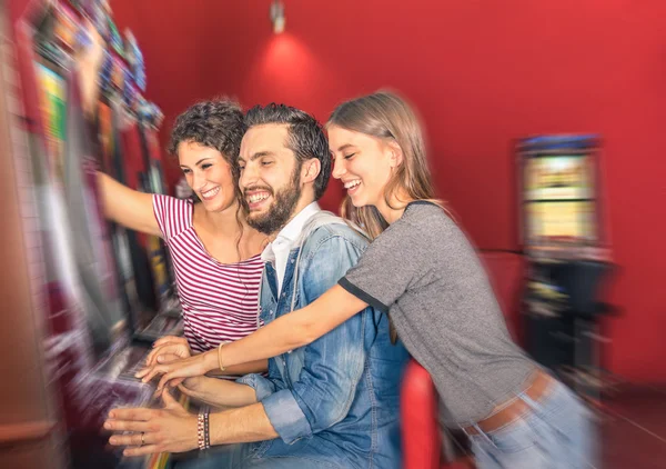Happy young friends having fun together with slot machine - Gambling concept with people playing at cash automatic devices in modern casino and resort - Blurred edges with soft radial zoom defocusing — Stock Photo, Image