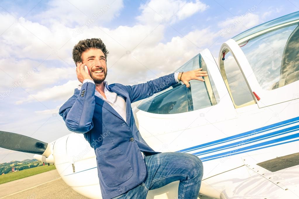 Young handsome man talking with mobile smart phone at private airplane - Modern business concept with confident guy using smartphone at airport - Modified paintings on air plane and tilted horizon