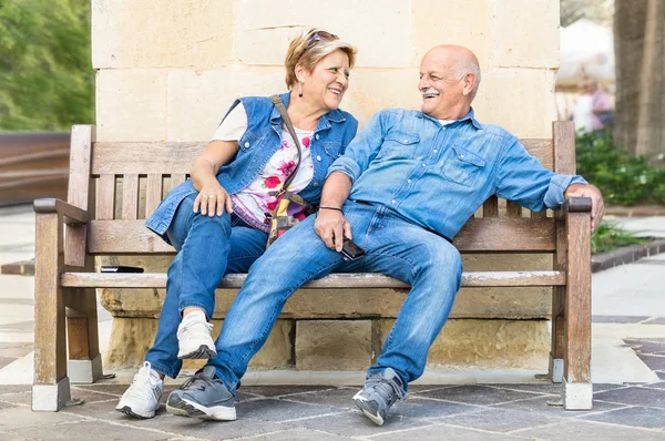 Happy senior couple having fun on a bench - Concept of active playful elderly during retirement - Everyday lifestyle in autumn sunny afternoon - Soft vintage filtered look with slightly blurred edges — Stock Photo, Image