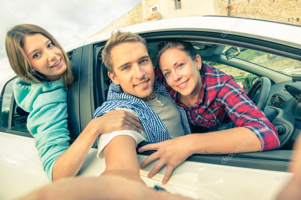 Handsome guy having fun with girlfriends - Best friends taking selfie at car trip on the road - Happy friendship and wanderlust concept with people traveling together - Soft vintage filtered look