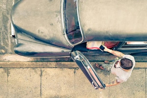 Joven hipster fashion man con tatuajes viendo smartphone junto a su coche vintage durante un viaje por carretera en Cuba - Concepto de nuevas tendencias y tecnología mezclada con estilo de vida retro - Aspecto nostálgico filtrado — Foto de Stock