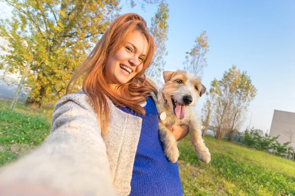 Unga rödhårig kvinna med selfie utomhus med söt hund - begreppet vänskap och kärlek med människor och djur tillsammans - solig vinter eftermiddag med varm färg toner - lutande horisonten sammansättning — Stockfoto