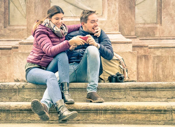 Pareja joven feliz divirtiéndose con el teléfono inteligente al aire libre - Citas y el concepto de coqueteo con los mejores amigos hipster interactuando con la nueva tecnología - Comienzo de una historia de amor en cálido aspecto filtrado vintage — Foto de Stock