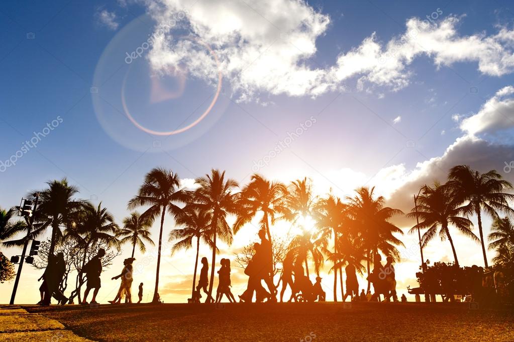 Silhouette of people walking at sunset on crowded Kalakawa Ave - Front walk street promenade of Waikiki Beach in Honolulu Hawaii - Enhanced sunlight warm filter with lens flare as part of composition